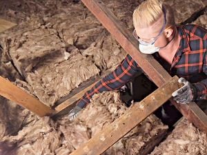 A man wears safety goggles, a mask and gloves while installing insulation.
