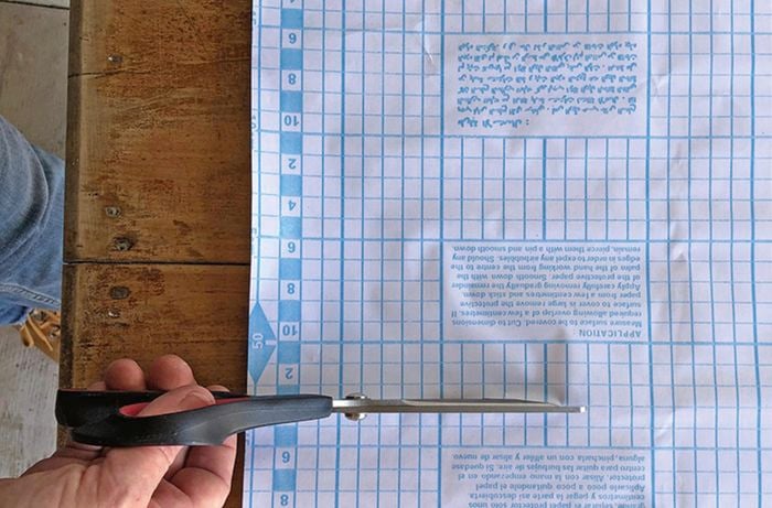 Person cutting a sheet of adhesive film with scissors