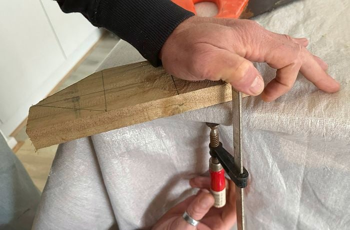 Hands holding and clamping a piece of timber to a workbench edge.