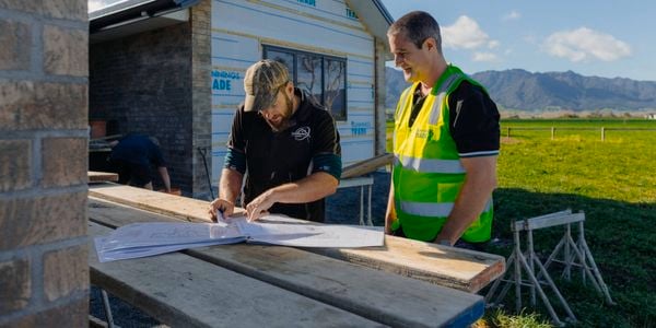 Man with fluro green top working with a builder and looking at a house plan