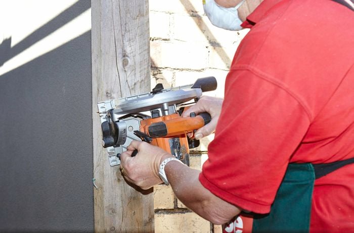 Person using power sander on timber plinth.
