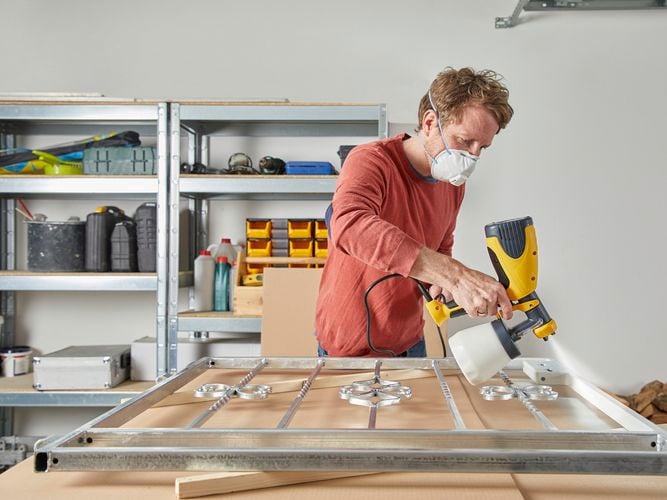 Wagner W100 Wood and Metal Sprayer spraying a metal fence with paint inside a garage.