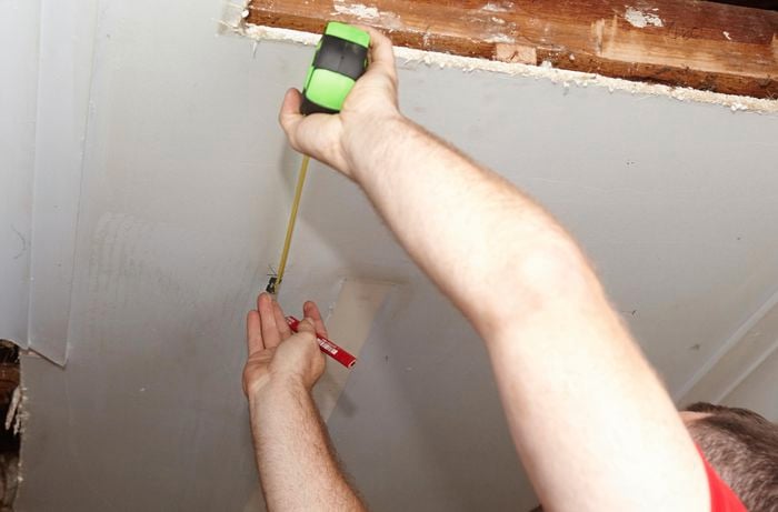 A person measuring across a ceiling from an exposed rafter