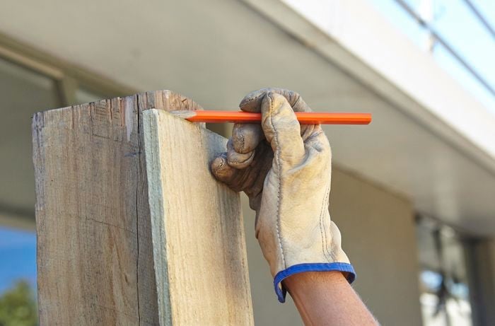 Person holding plinth against post and making a mark with pencil.