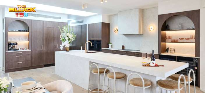 Contemporary kitchen featuring a large stone island bench, dark timber cabinetry, arched display shelving and bar stools.