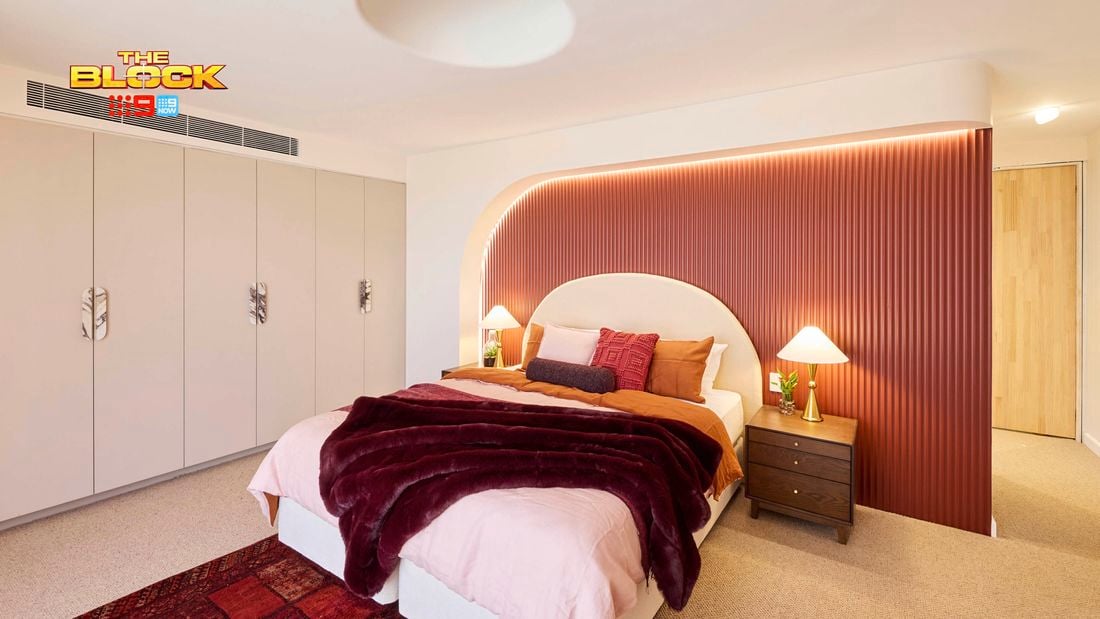 Bedroom with red feature wall, arch lighting, and layered bedding in warm tones.