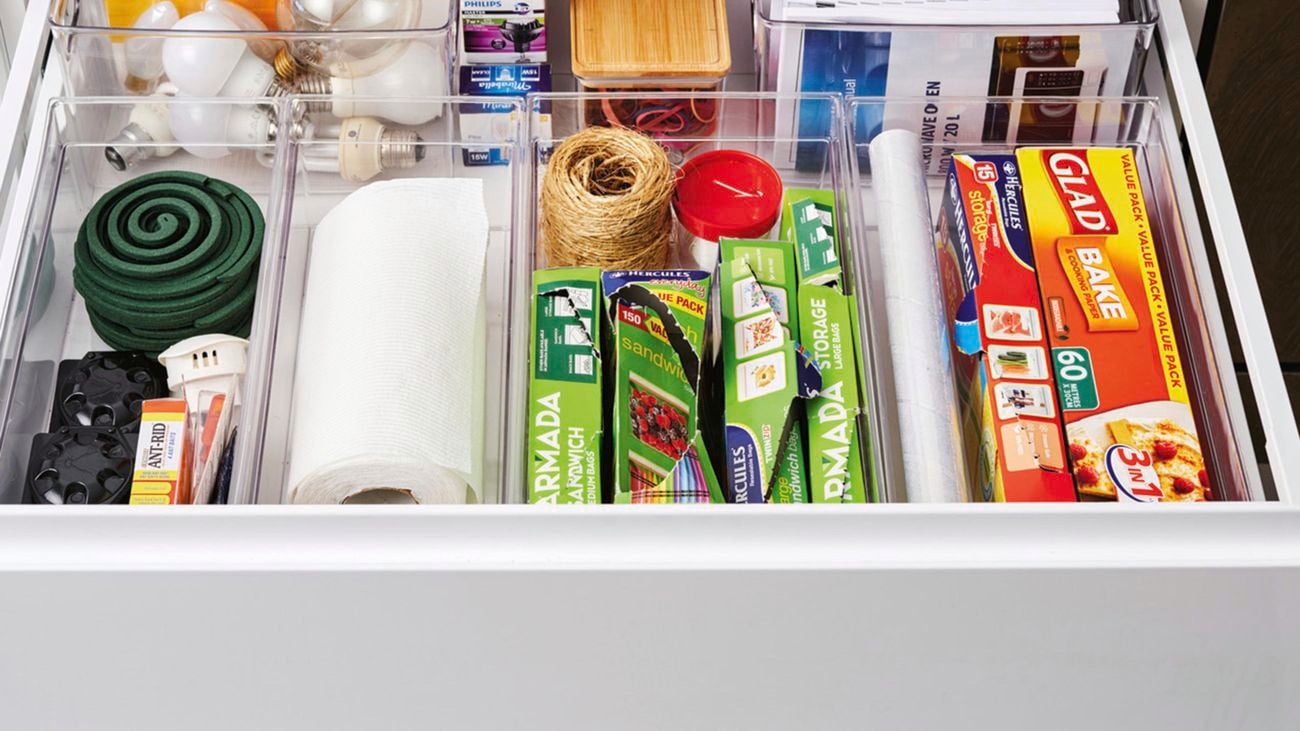 Organised drawer containing dividing clear drawers of glad wrap, paper towel, baking paper, recipe books and general accessories.