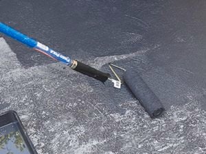 A driveway being painted black with a paint roller