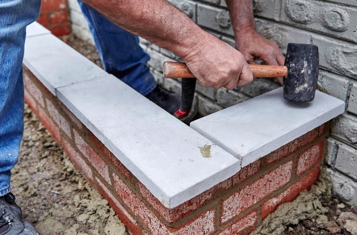 A person using a mallet to tap concrete capping blocks into position