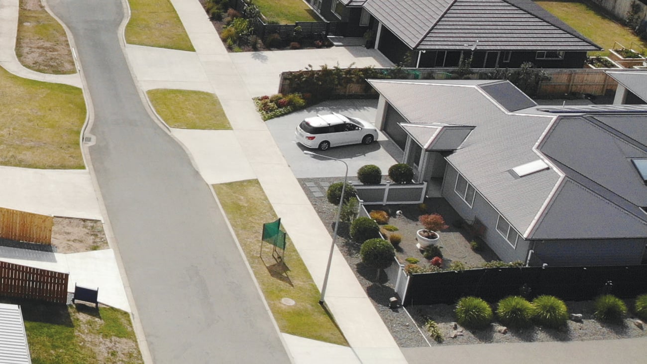 Aerial shot of the framework of a house, with empty lots, a lake and a soccer pitch in the distance