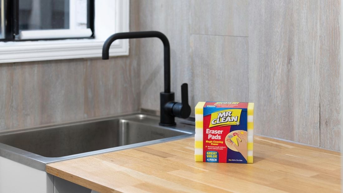 A packet of four magic erasers sitting on a wooden benchtop in front of a sink