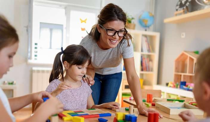 indoor play centre with lady and three children playing with colourful blocks.
