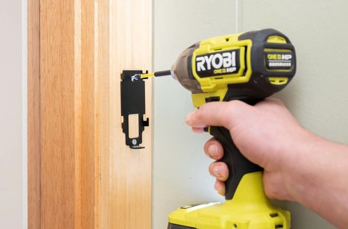 A person is mounting a bracket onto a wooden door frame using a power drill.