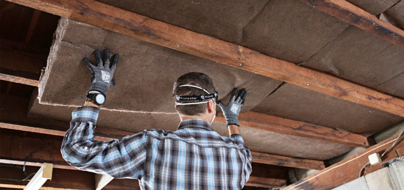 Man wearing face mask and gloves (PPE) is standing on ladder to install ceiling insulation
