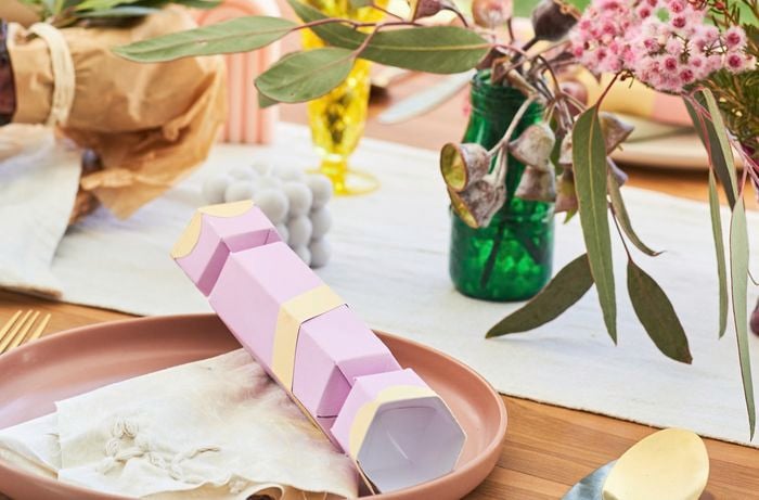 An outdoor table is decorated with a Christmas cracker and flower.