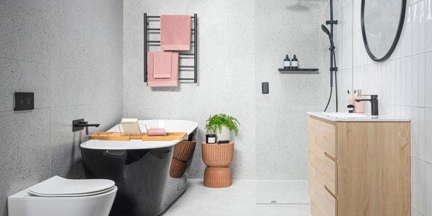 Bright bathroom with black bath tub, towel rail and tapware and terrazzo shower wall and toilet.