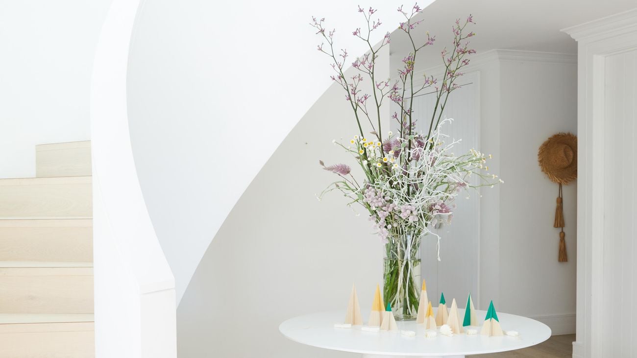 Homemade paper decorations sit on top of a circular table with a vase of purple flowers