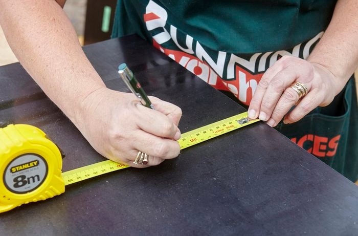 A person marking a measurement onto formply