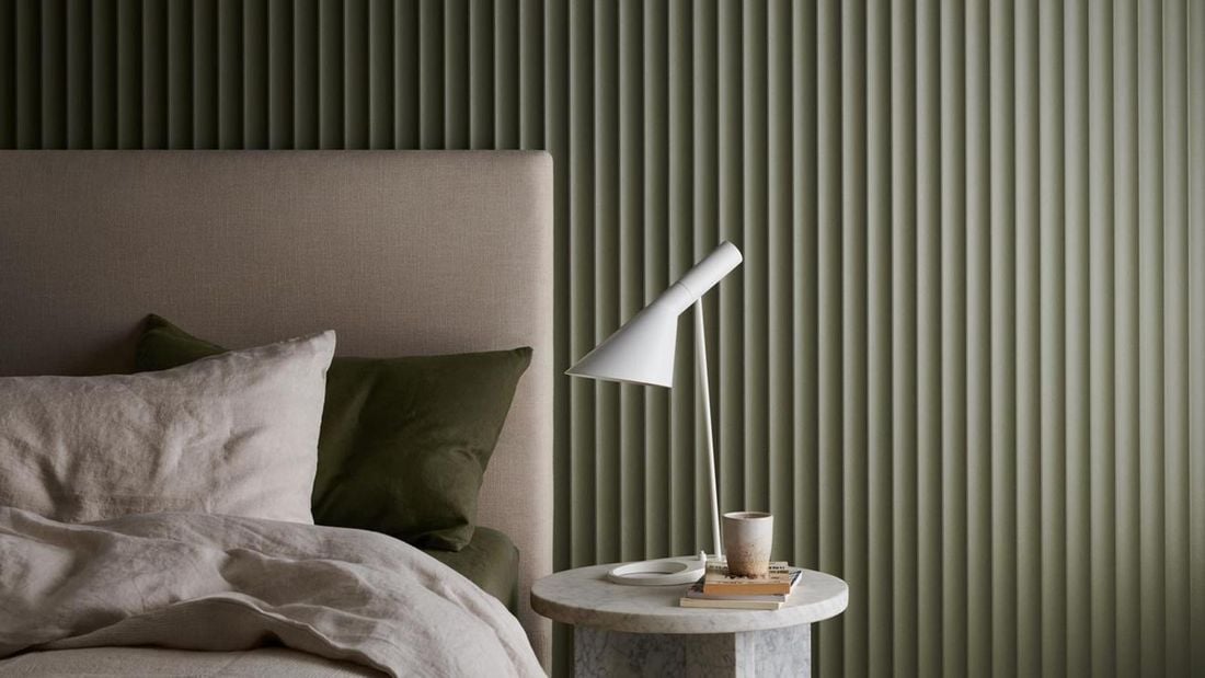 Bedroom with a bed and bedhead, pillows, bed linen, marble look side table and white lamp. Scallop 45 design in Dulux Gully.