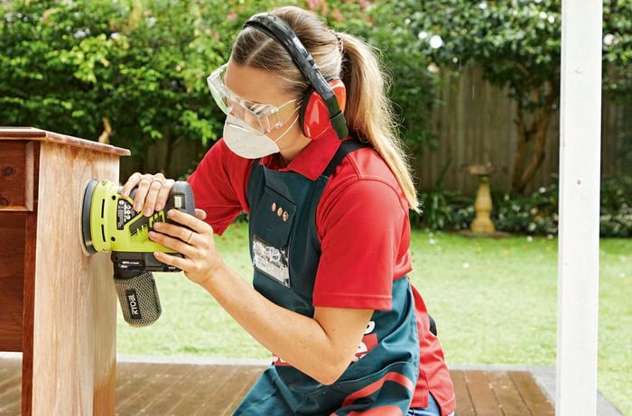 A person using a Ryobi orbital sander to sand down an old timber desk.