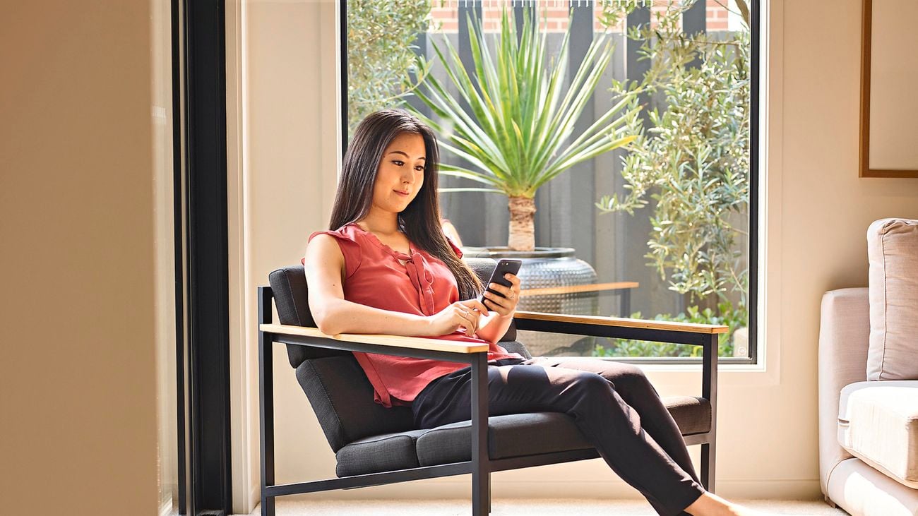 A woman sits on a black armchair while using a smartphone