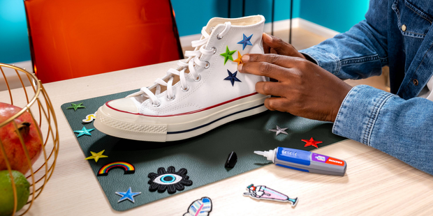 Person attaching decorative patches to a white sneaker using a Loctite craft adhesive pen