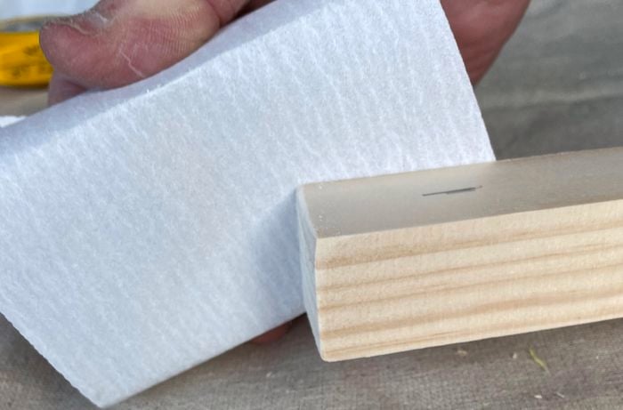A person sands down the edges of a pine piece.