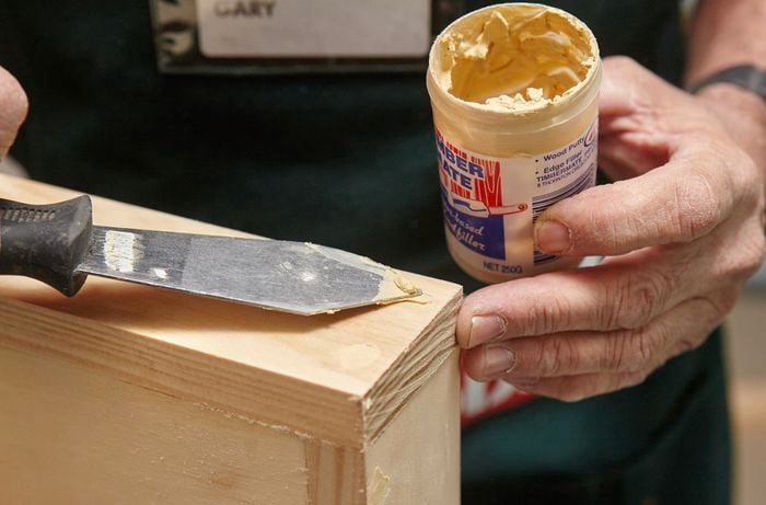 A person filling a hole in timber with wood filler using a putty knife