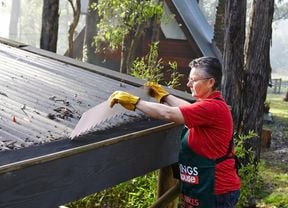 Person fitting gutter guard to a roof in a bushland setting