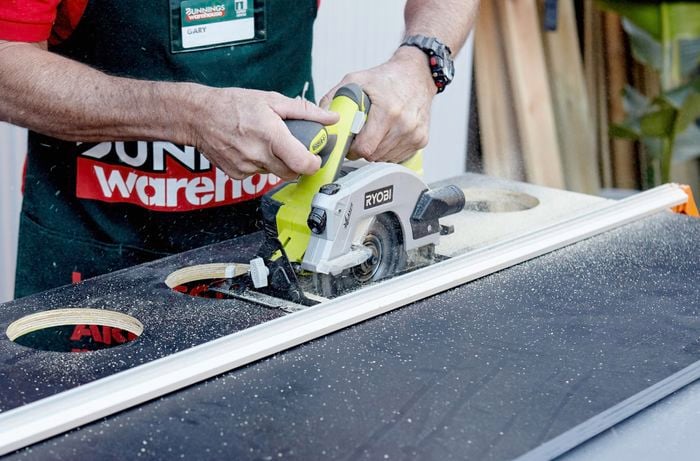 A circular saw cutting through a piece of particle board painted black with a hole in the centre