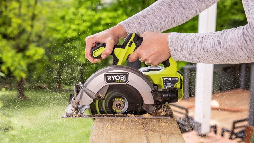 A person operating a circular saw to cut a plank.