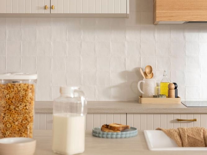 A kitchen with beige kitchen cupboards, a white splashback, brown benchtops with crockery on it.