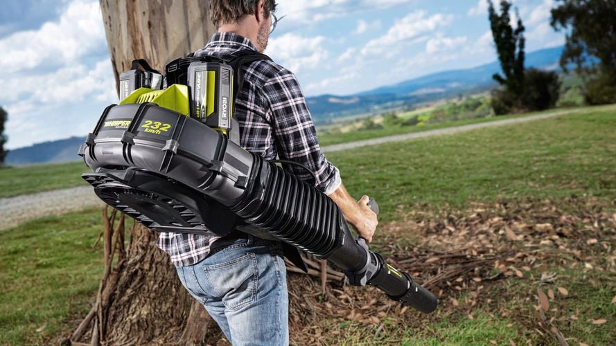 An individual blowing leaves in a garden using a cordless backpack blower.