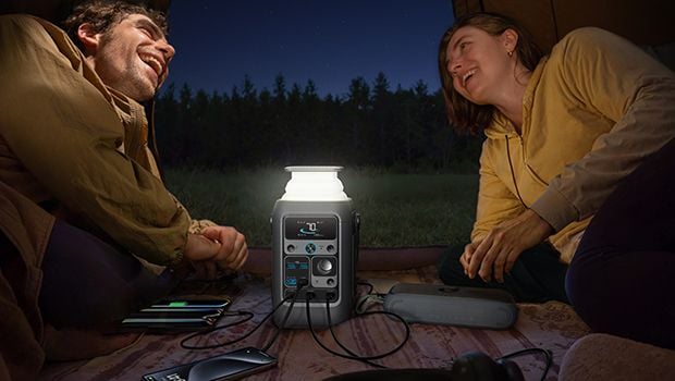 a couple camping outdoors while having a portable power station next to them