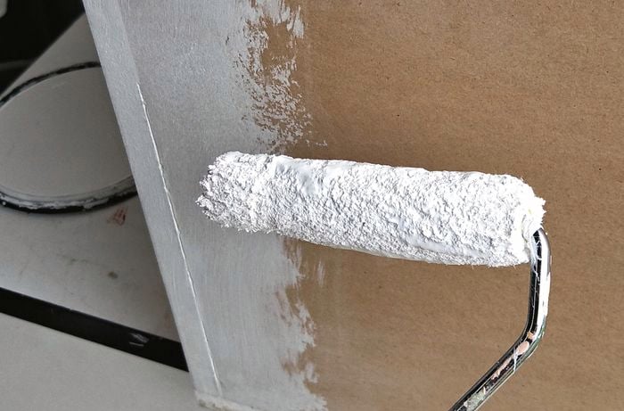 Paint roller applying white paint to cabinet.