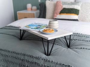 White painted bed tray topped with a magazine, danish on a plate and mug on a made up bed