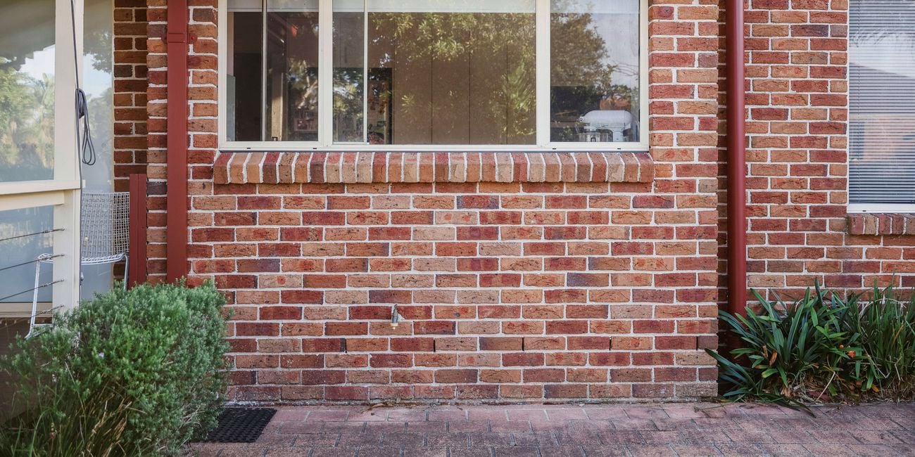 An exterior brick house wall with a window, showing the area where a raised dog-wash station has been removed.