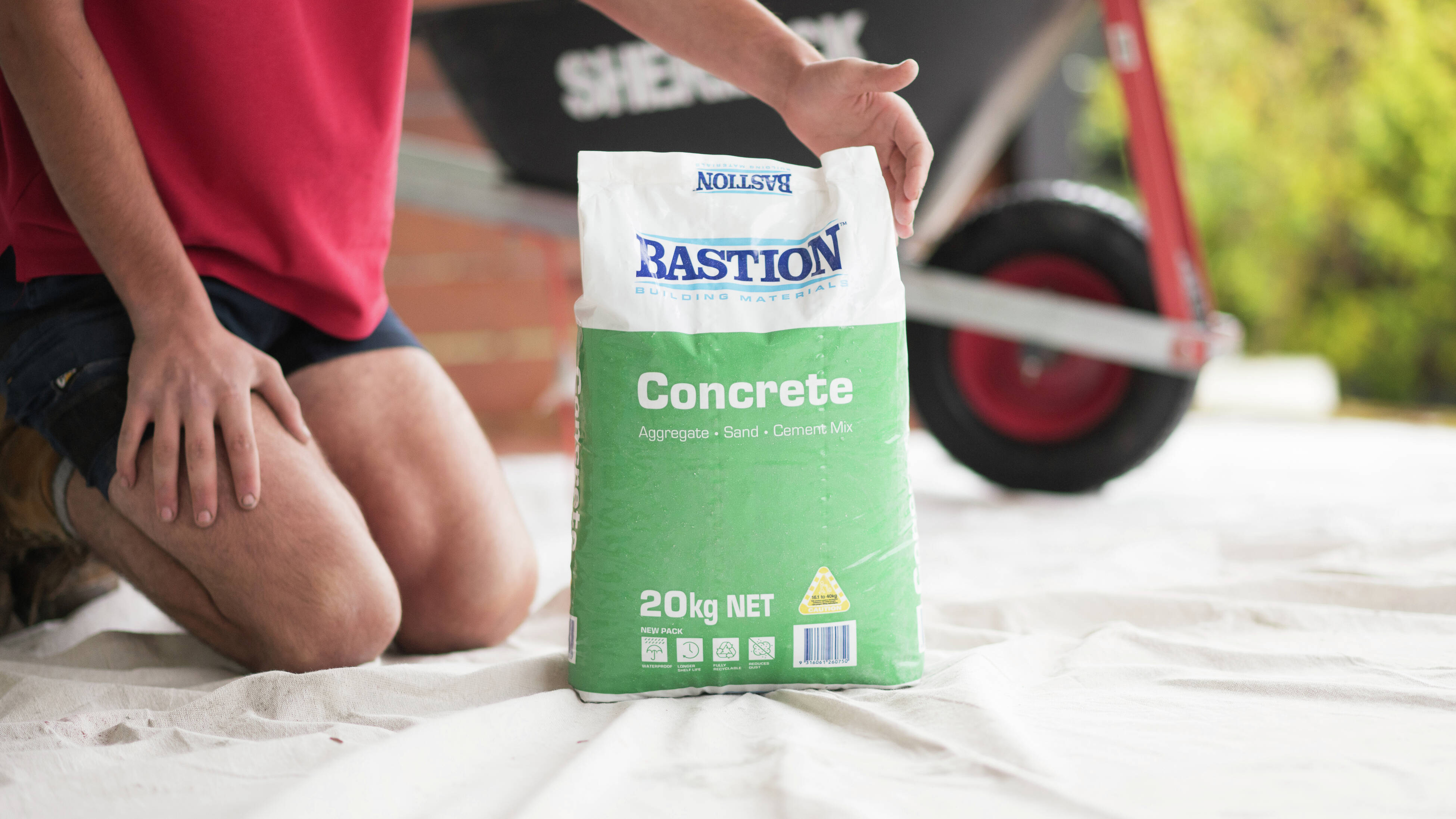 A person is sitting with a bag of Bastion concrete mix.
