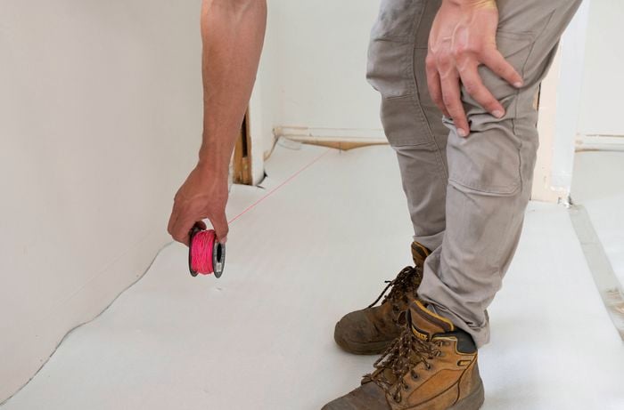 A person in work boots is holding a reel of pink stringline tied to a nail at one end.