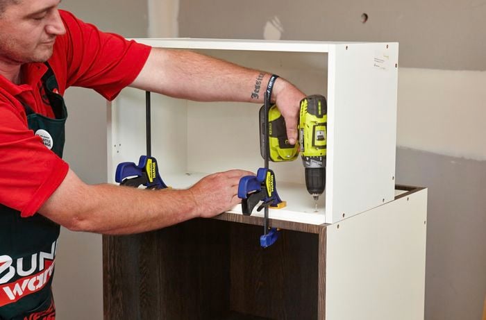 A person attaching two cabinet units using a clamp and cordless driver