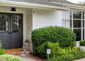 Front entrance of a suburban house with a doorbell camera, home security camera, front porch and shrubs.