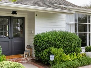 Front entrance of a suburban house with a doorbell camera, home security camera, front porch and shrubs.