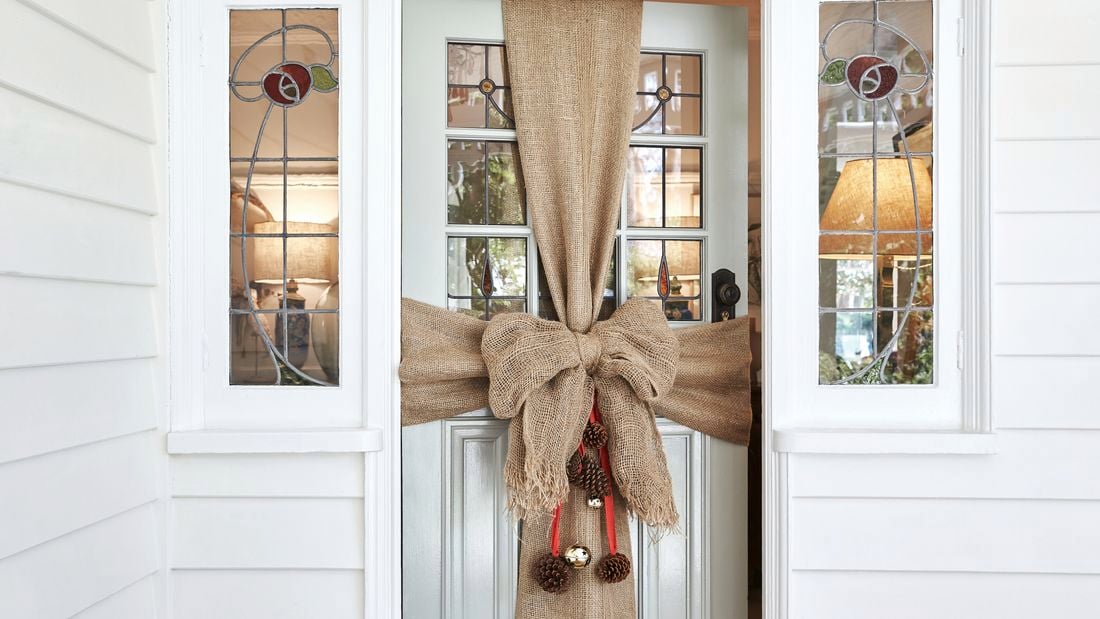 Large hessian bow wrapped like a present around the front door with pinecones and baubles hanging from the centre.