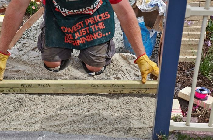 A person holding a length of timber with levels marked on it across the sand base of a pathway