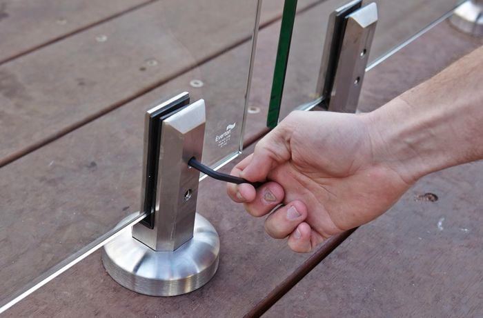 Person tightening screws in mini post to secure pool glass fencing.
