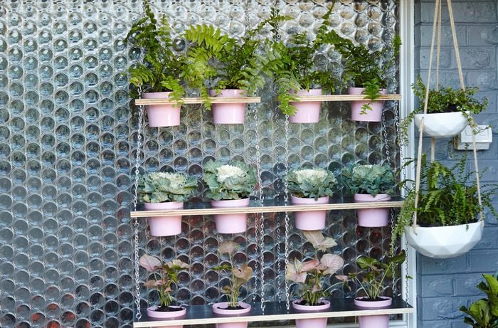 A completed vertical garden with three tiers, each tier holding four pink plant pots, in front of a circular patterned glass window pane