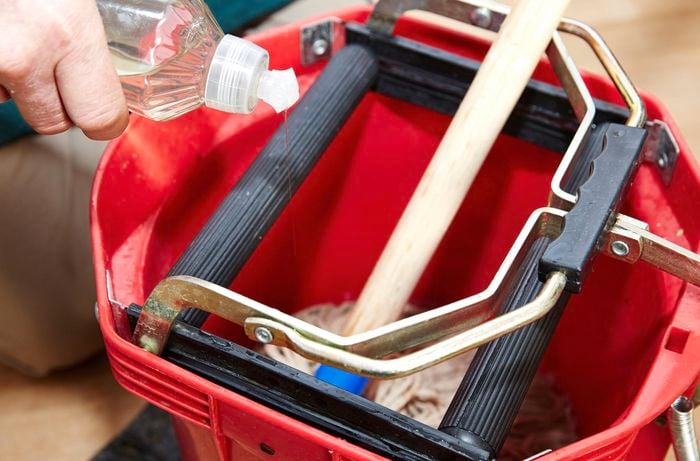 A person adding detergent to a mop bucket
