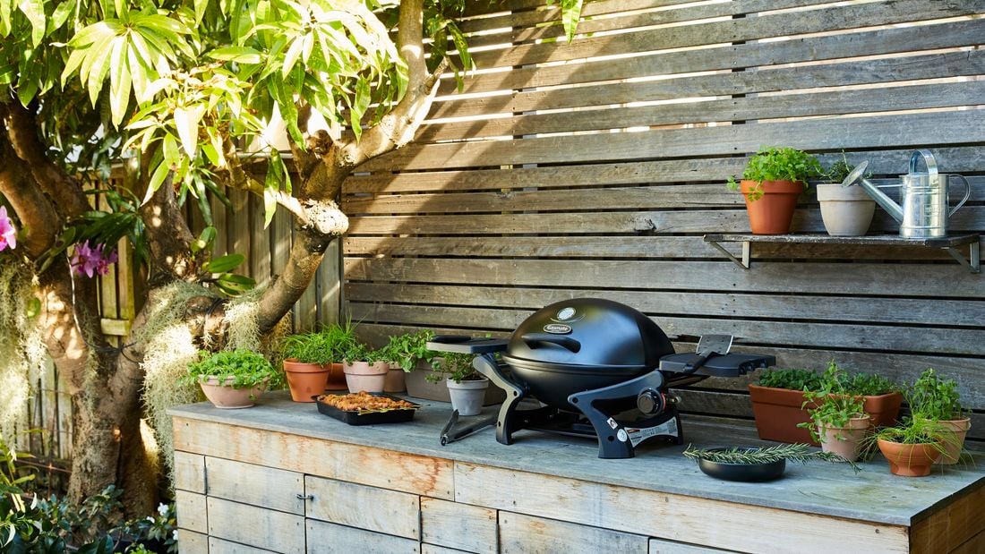 A portable barbecue in an outdoor setting surrounded by pot plants with herbs