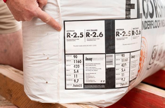 The image shows a person pointing to the R-2.5 rating on a pack of underfloor insulation.