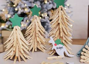 A cardboard kangaroo Christmas table place card with the name ‘Bridget’ written on it, resting in front of miniature wooden peg Christmas trees.